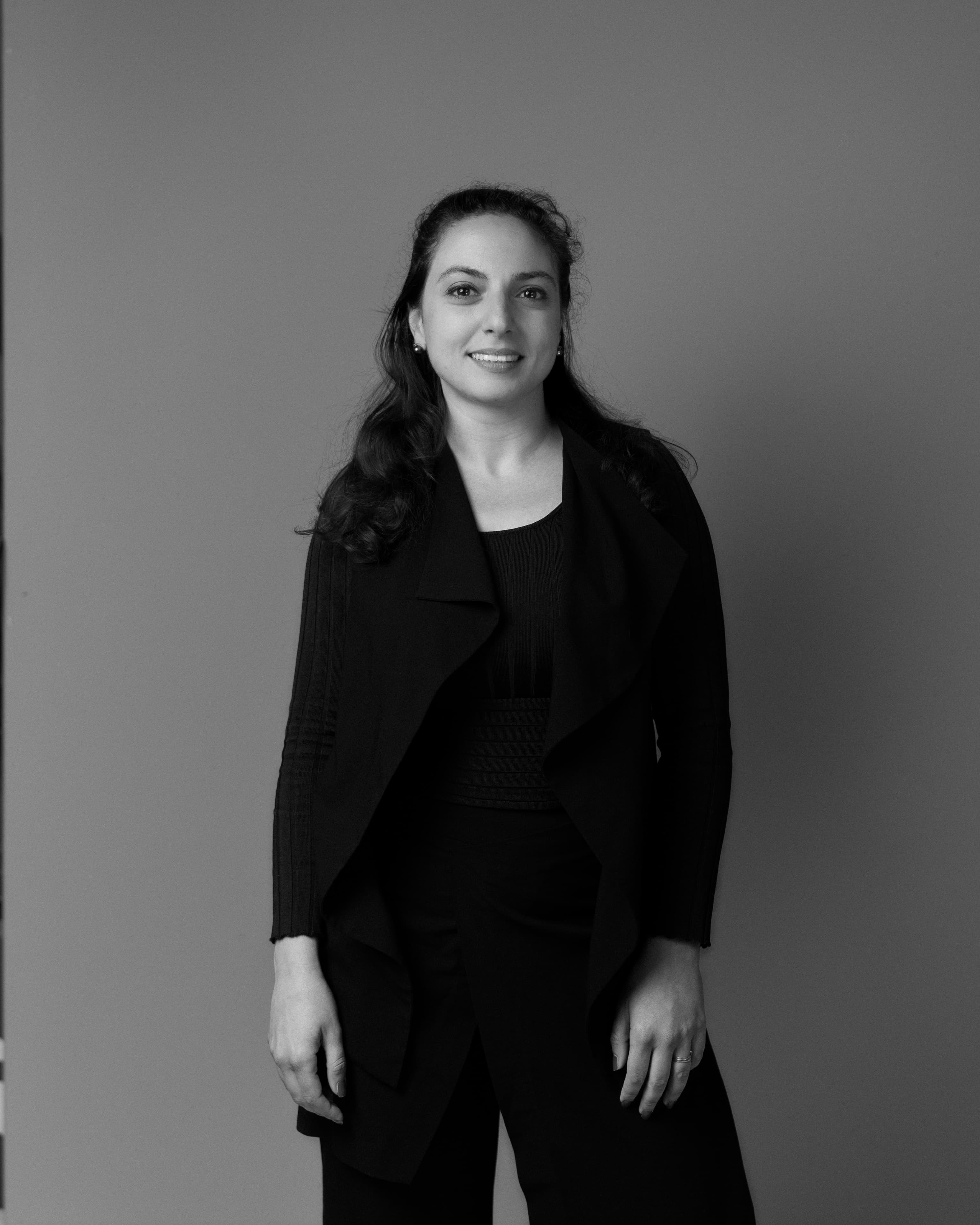 Portrait of a woman in a draped black blazer against a grey backdrop
