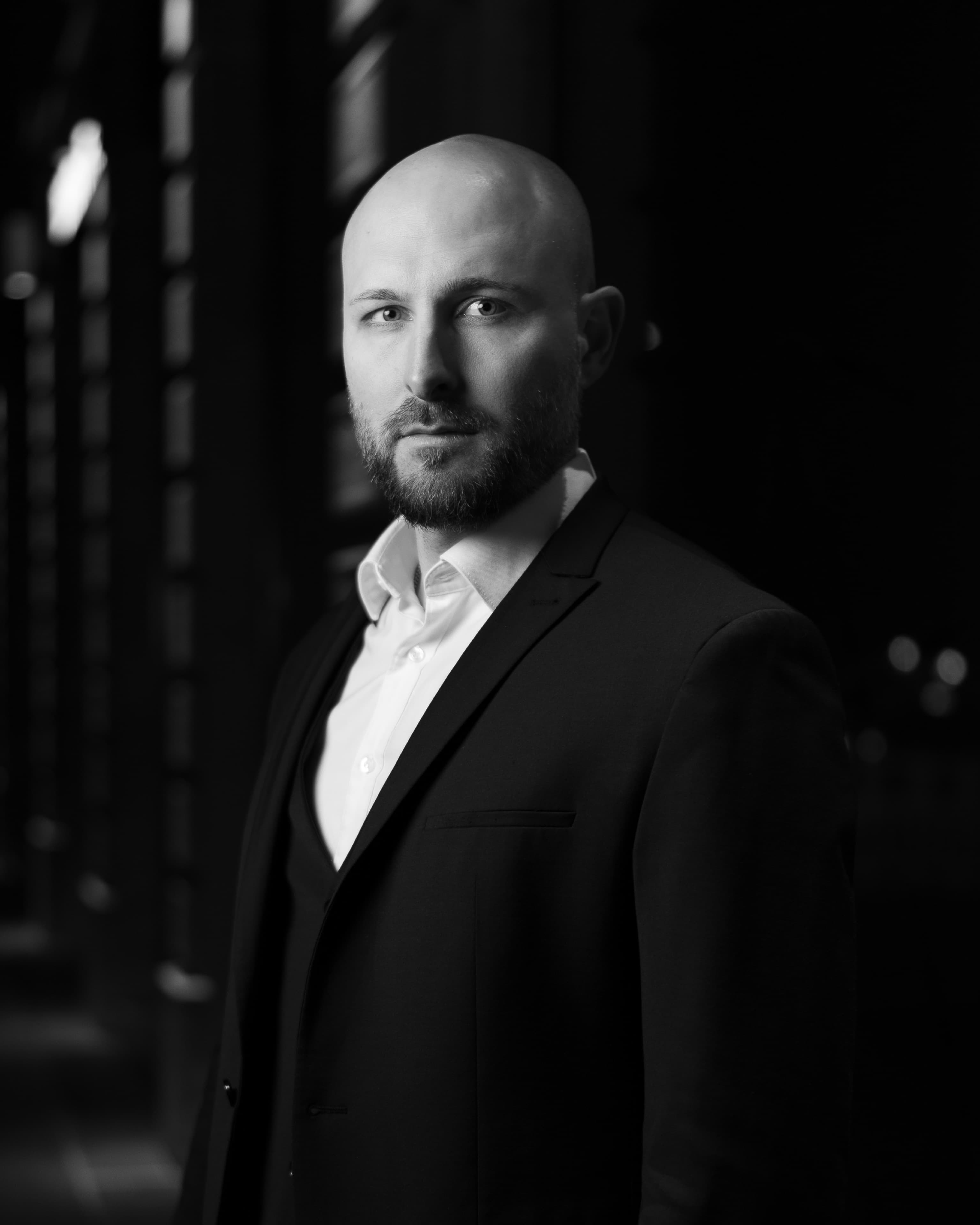 Dramatic black and white portrait of a bald bearded man in a three-piece suit