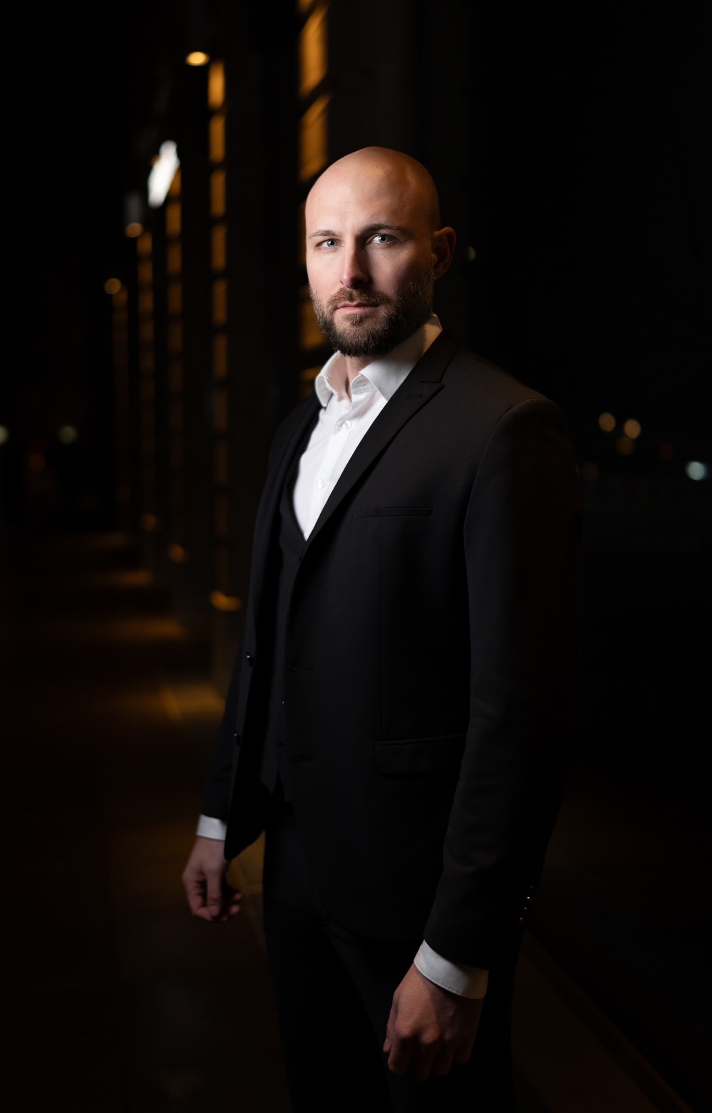 Black and white nocturnal portrait of a man in a suit beneath architectural columns