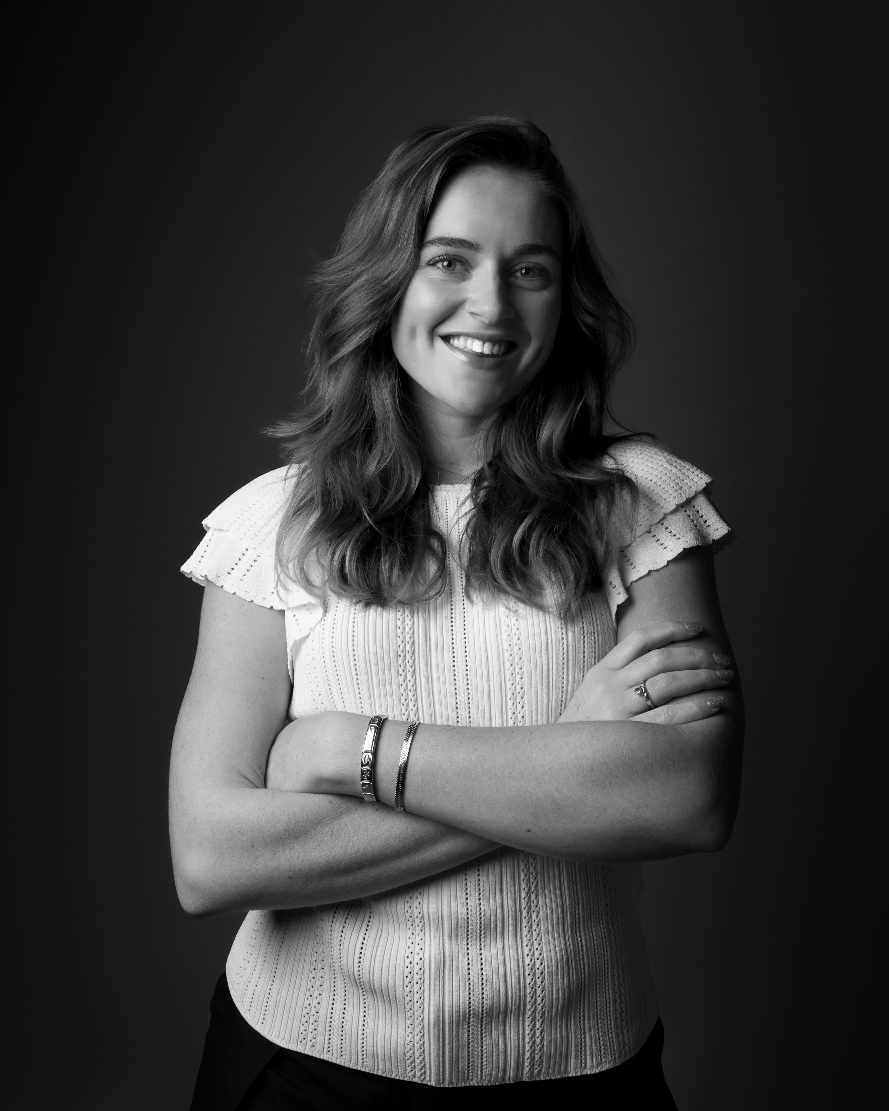Black and white studio portrait of a woman with arms crossed, soft smile