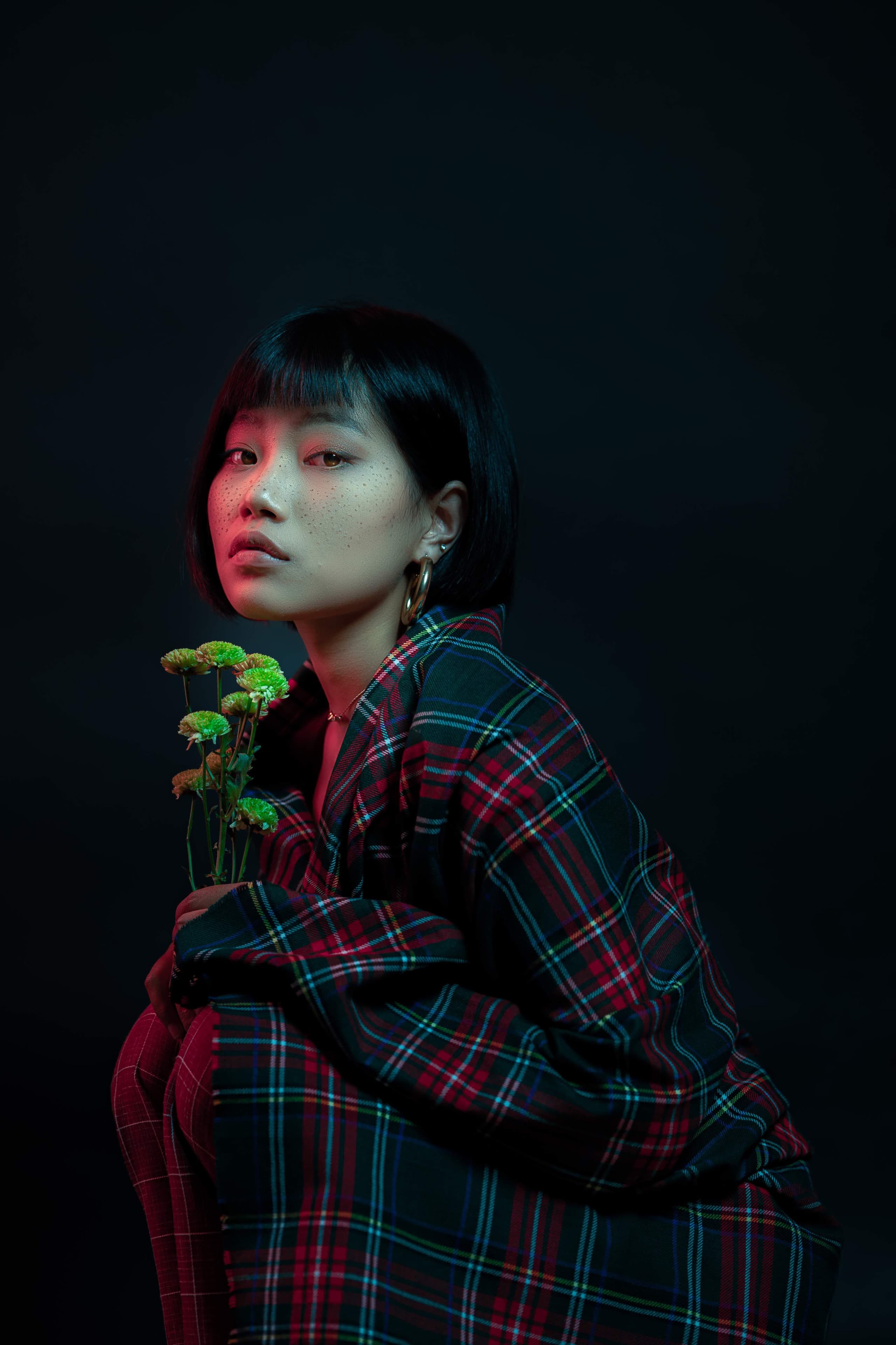 Editorial portrait of a model in tartan holding green blooms under coloured light