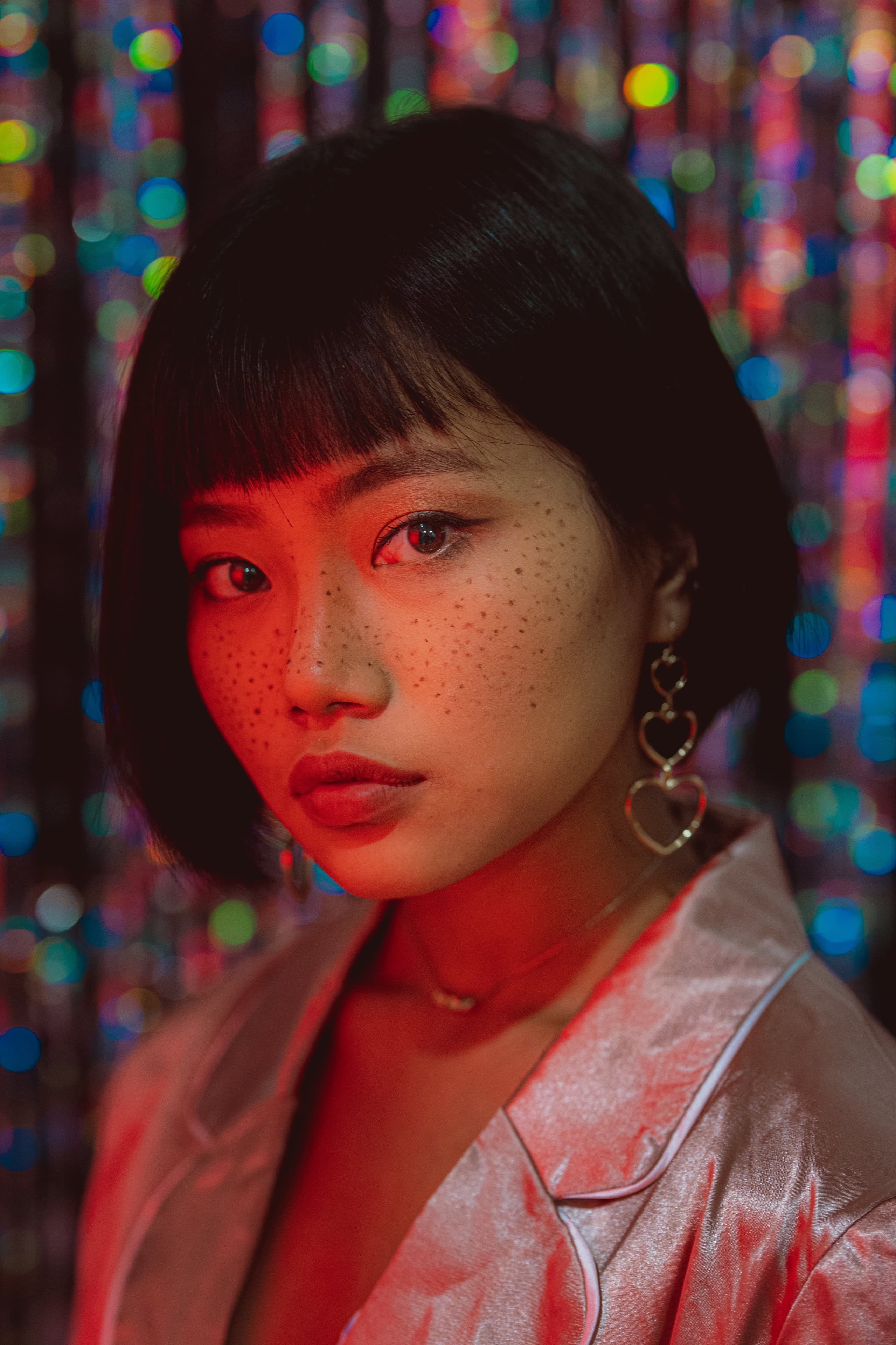 Editorial beauty portrait of a model in satin, freckles lit by warm gel against bokeh