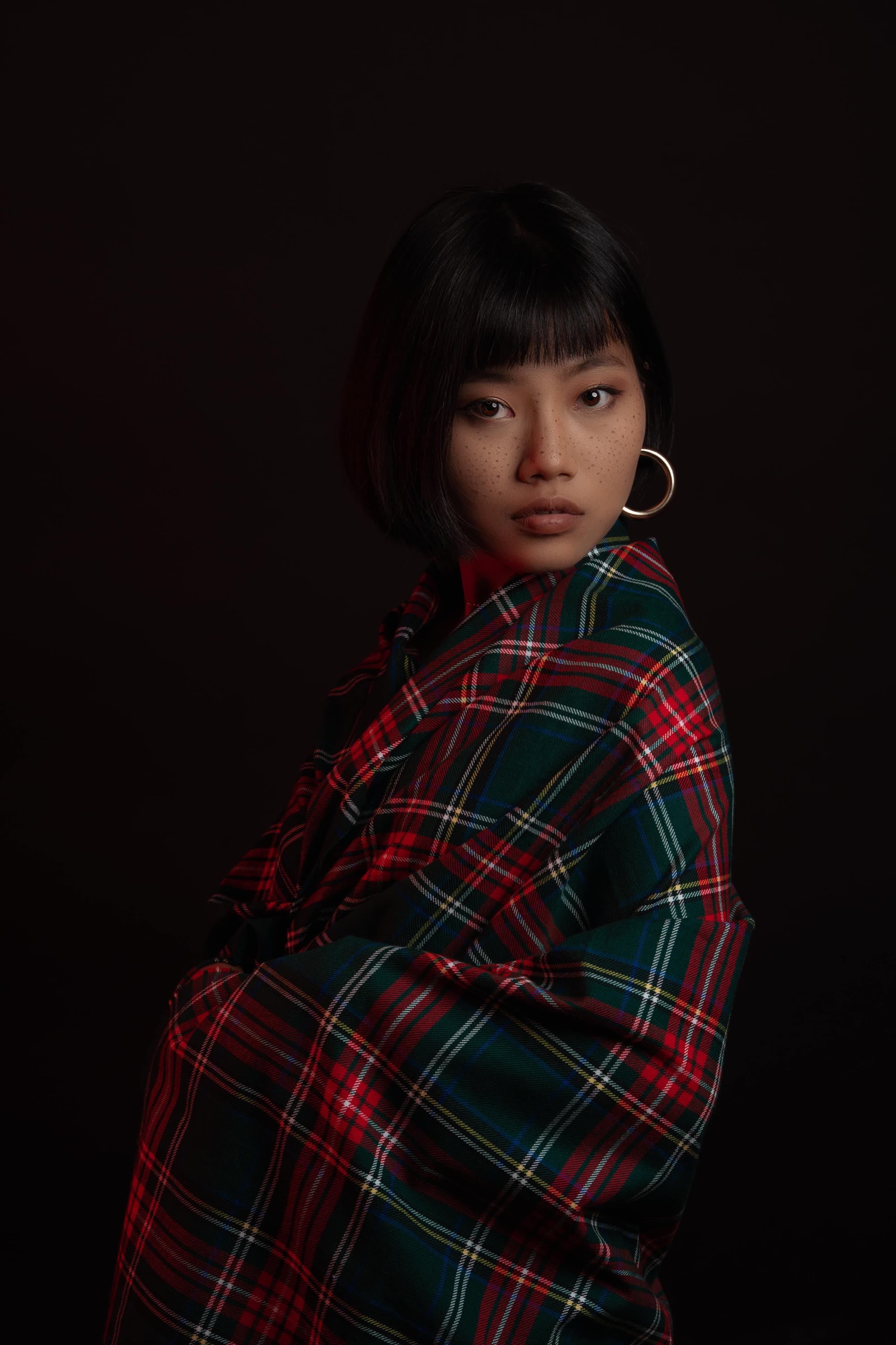 Editorial portrait of a model draped in tartan, turned to the side in low light