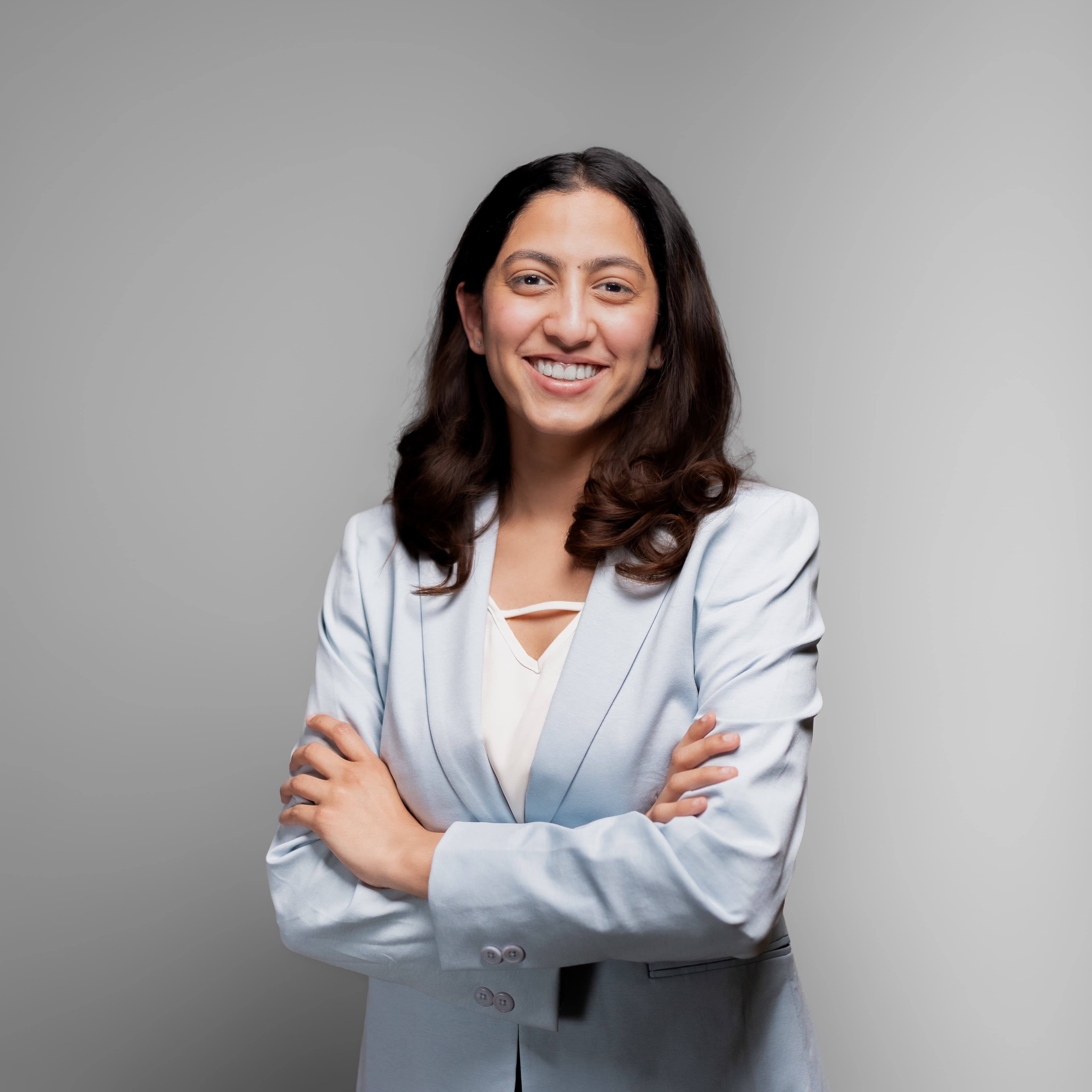 Corporate portrait of a smiling woman in a pale blue blazer, arms crossed