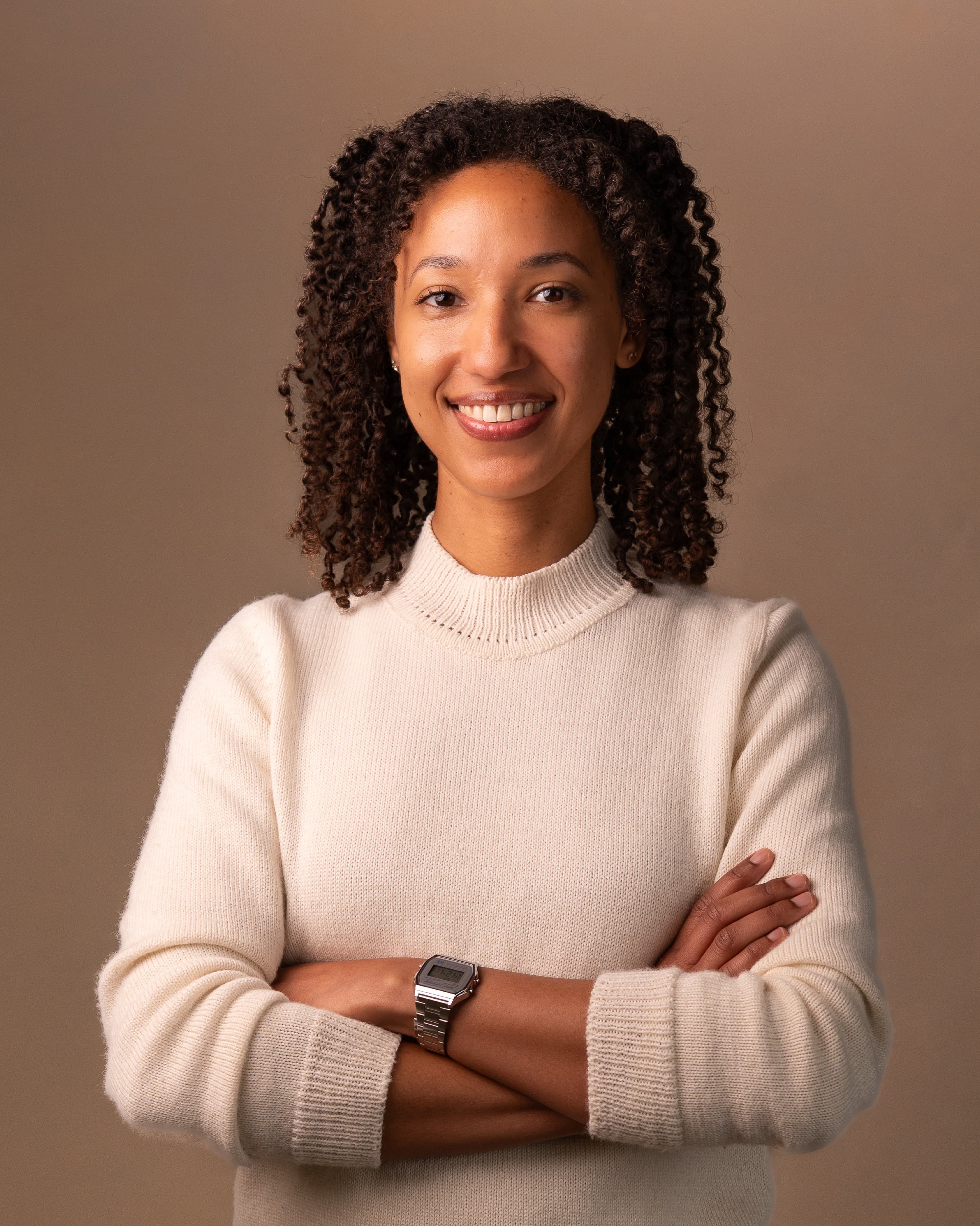 Executive headshot of a woman in a cream turtleneck against a warm tan backdrop