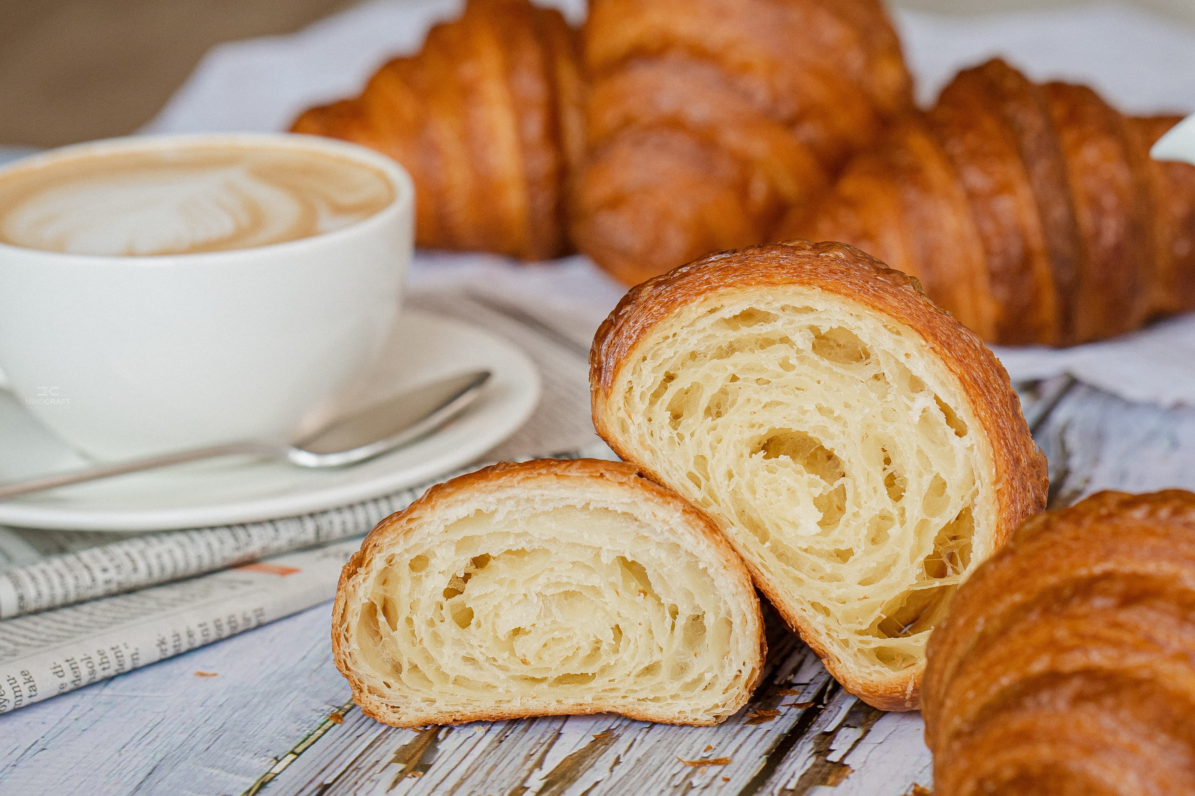 Butter croissants beside a flat-white, one sliced to reveal a laminated crumb