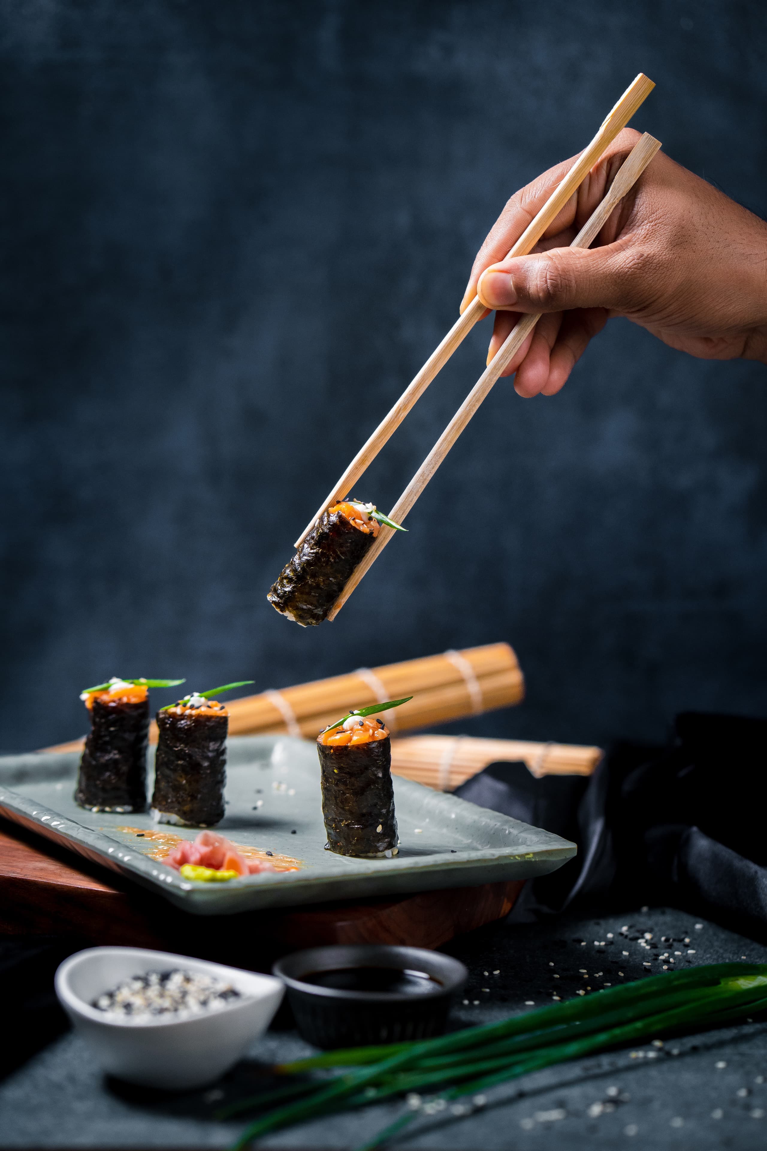 Salmon nori rolls lifted with chopsticks on a dark set