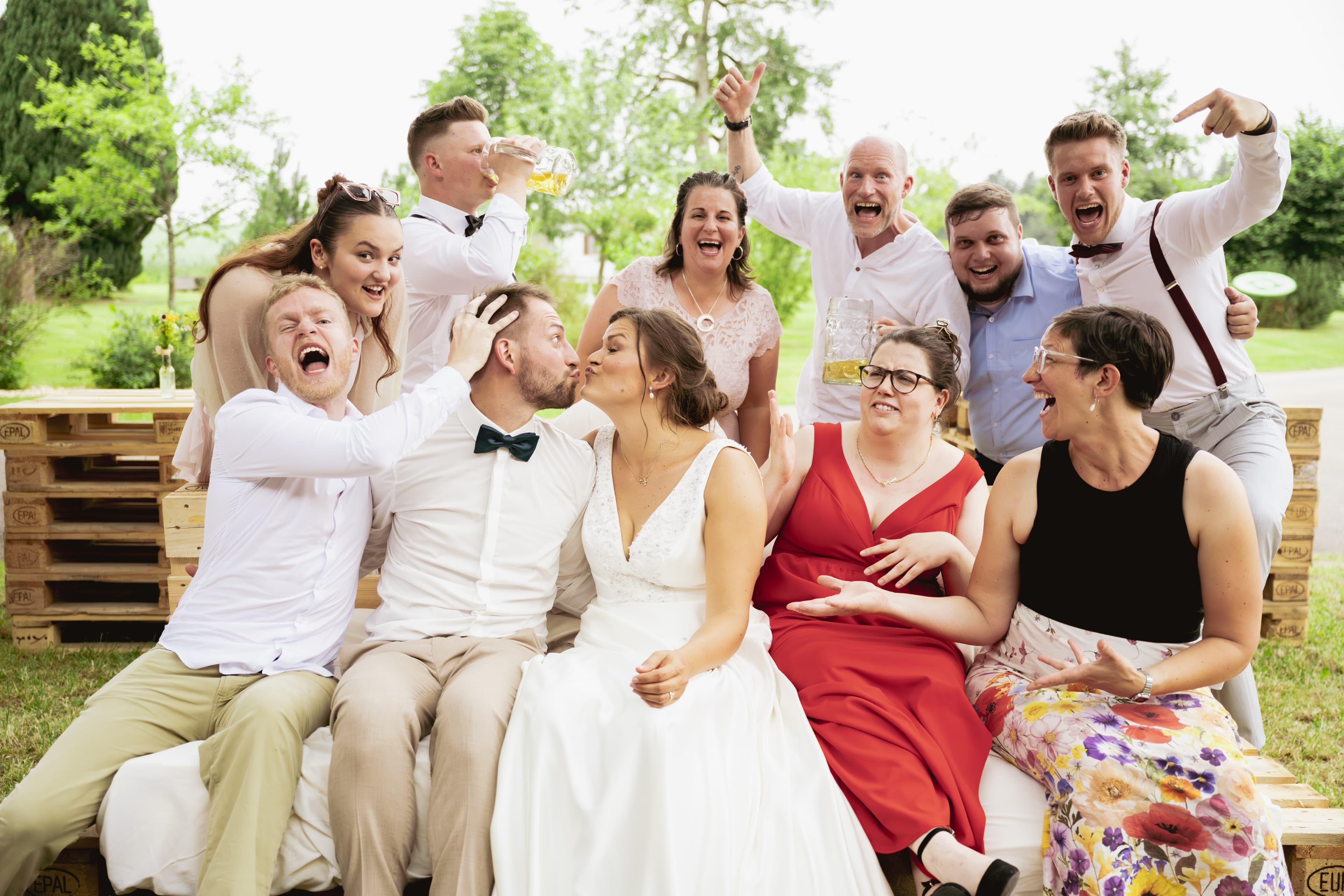 Wedding party crowded together laughing on a garden bench
