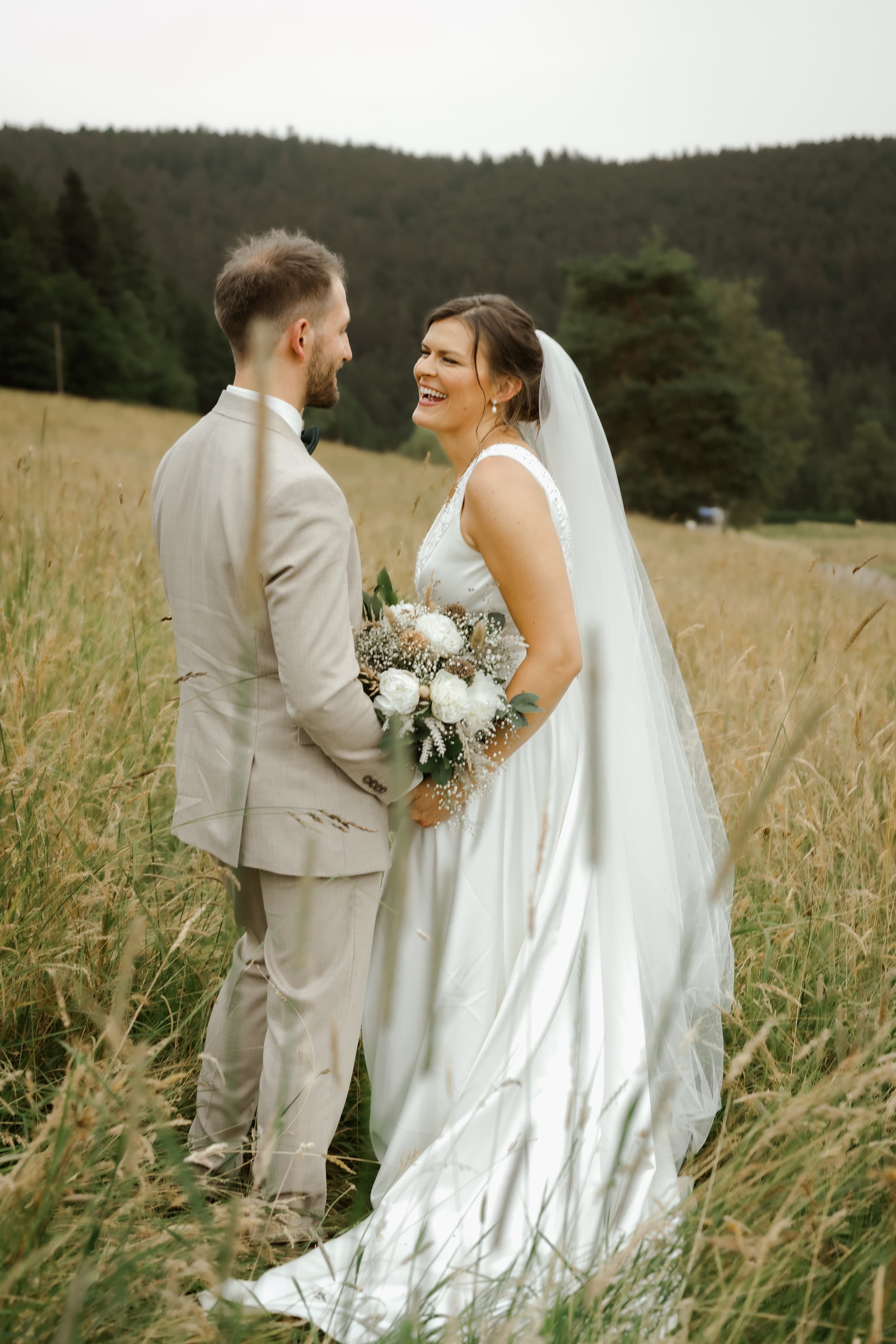 Bride and groom laughing together in a golden mountain meadow
