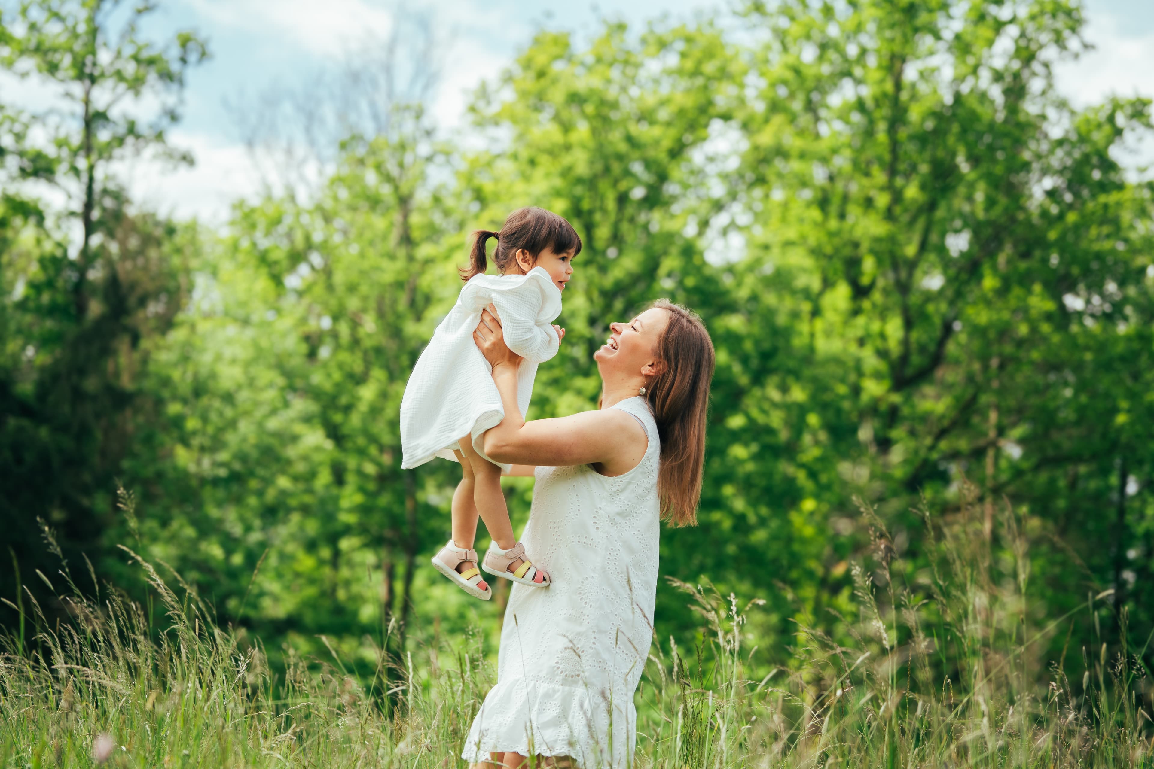 Mother lifting her daughter in a sunlit summer meadow