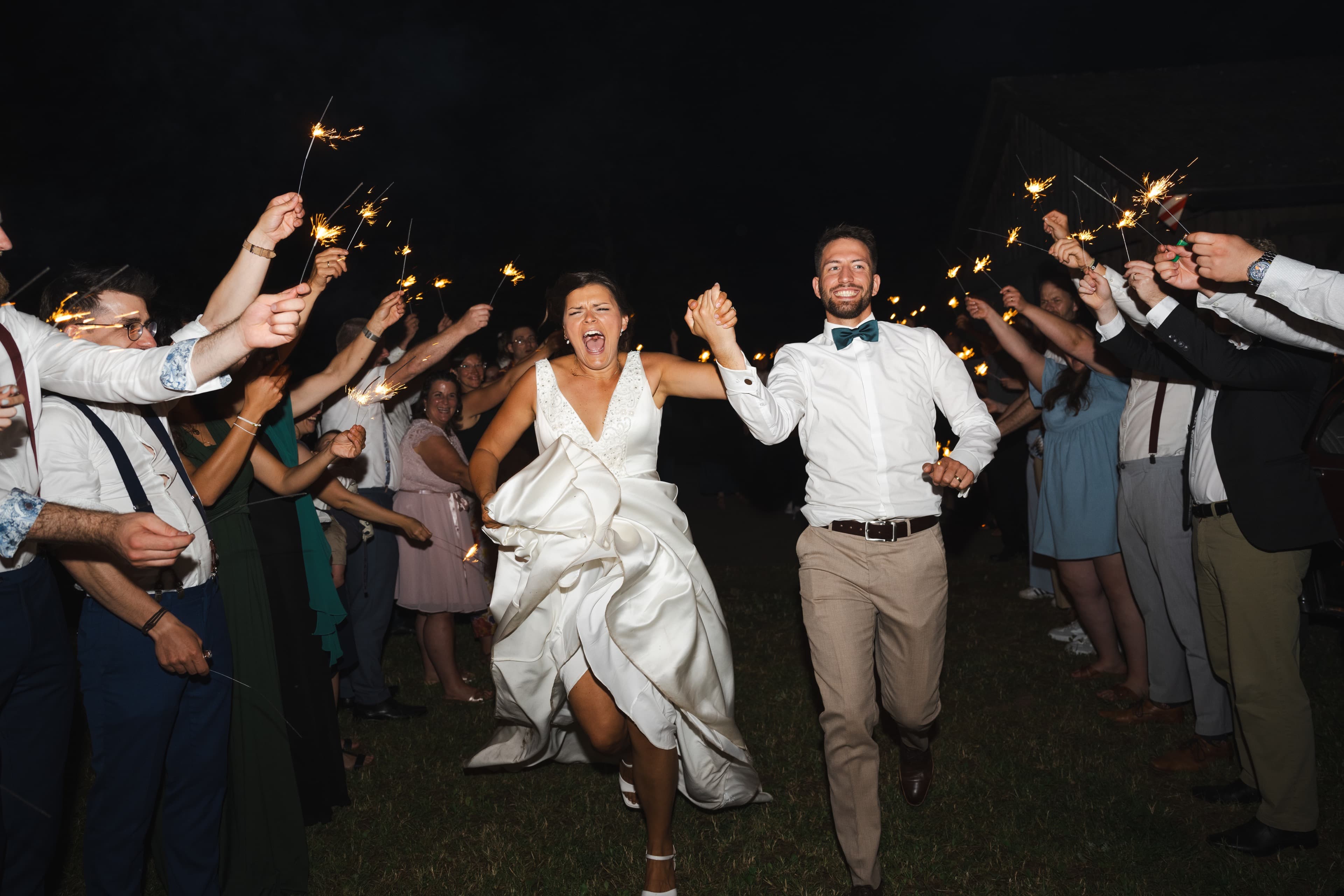 Night-time wedding sparkler exit, couple running through a tunnel of guests