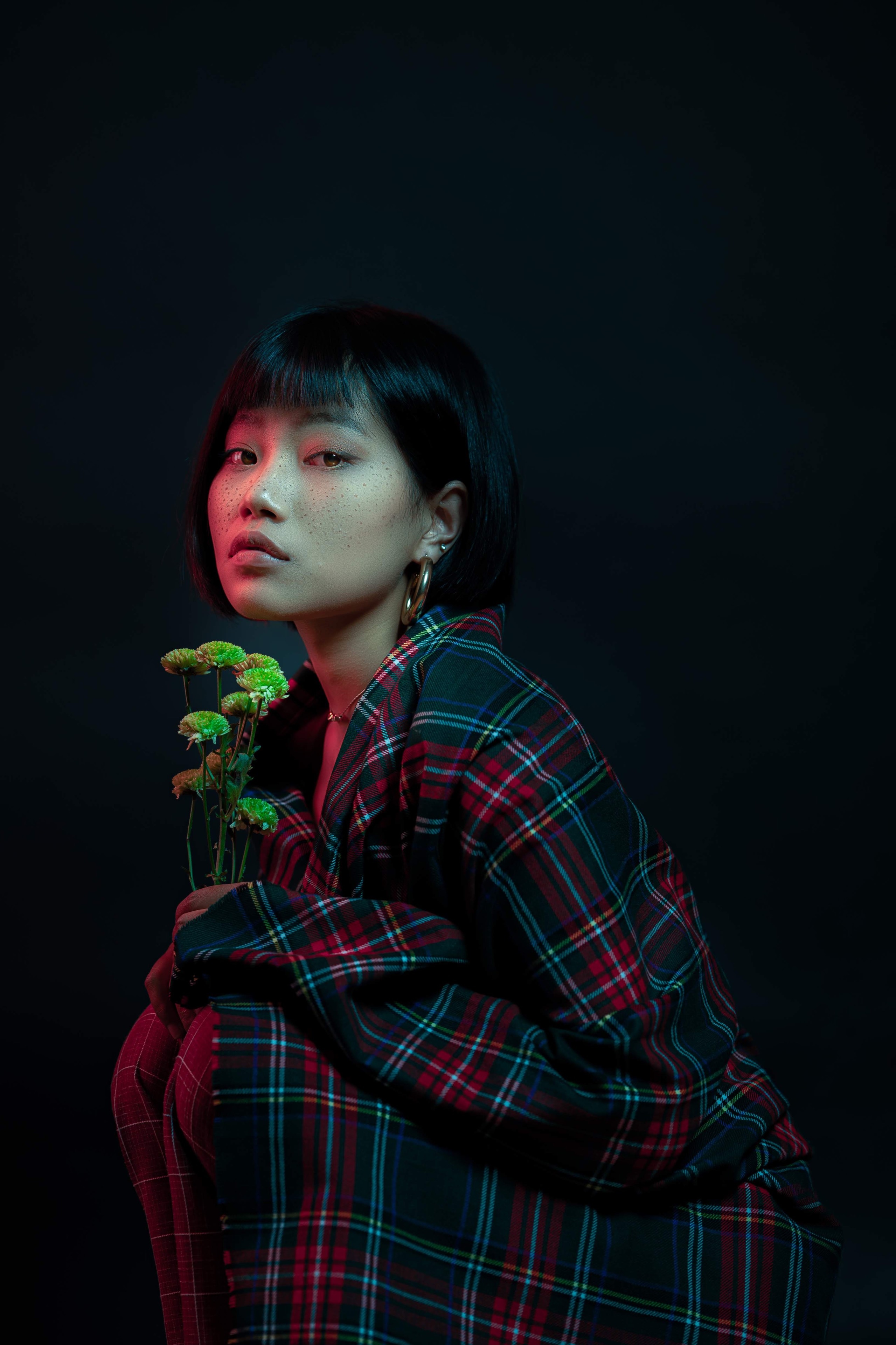 Editorial portrait of a model in tartan holding green blooms under coloured light